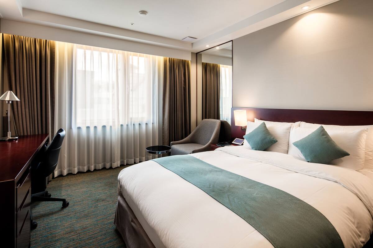 A hotel room with a large bed, a desk, a chair, and a lamp.
