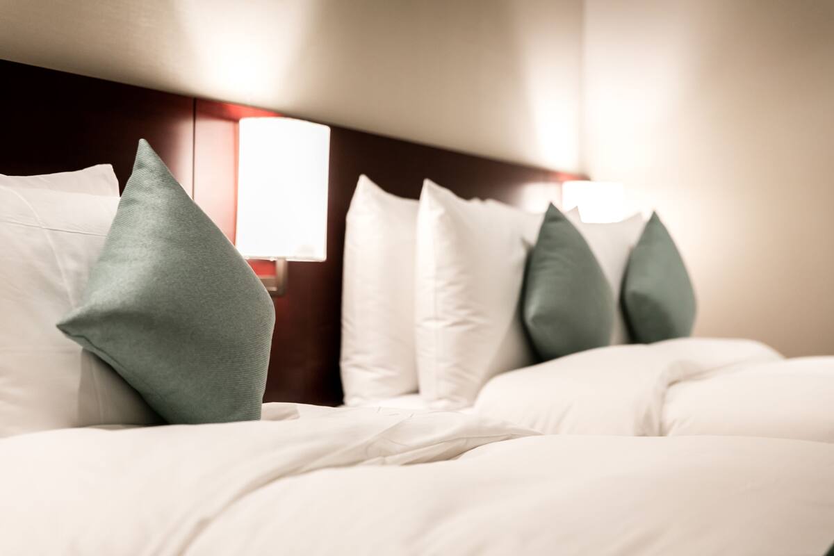 A neatly made bed with white and green pillows, a wooden headboard, and a wall-mounted light fixture.