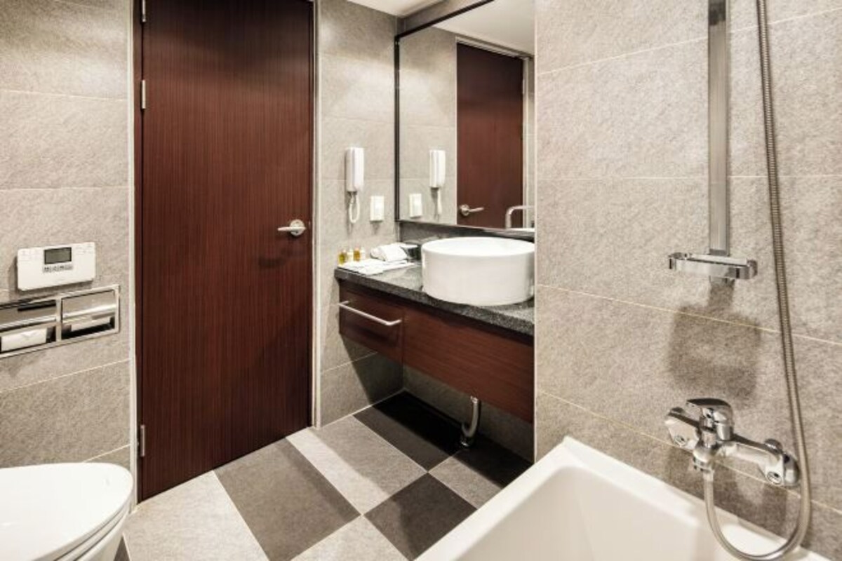 A modern bathroom with a toilet, sink, and bathtub. There is a mirror above the sink and a showerhead above the bathtub.