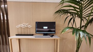 A wooden desk with a computer monitor, keyboard, and mouse. There is a potted plant and a fire extinguisher on the floor. - Hotel Sunshine Seoul (Seoul)