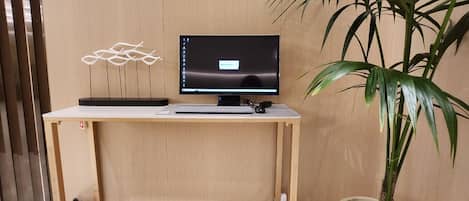 A wooden desk with a computer monitor, keyboard, and mouse. There is a potted plant and a fire extinguisher on the floor.