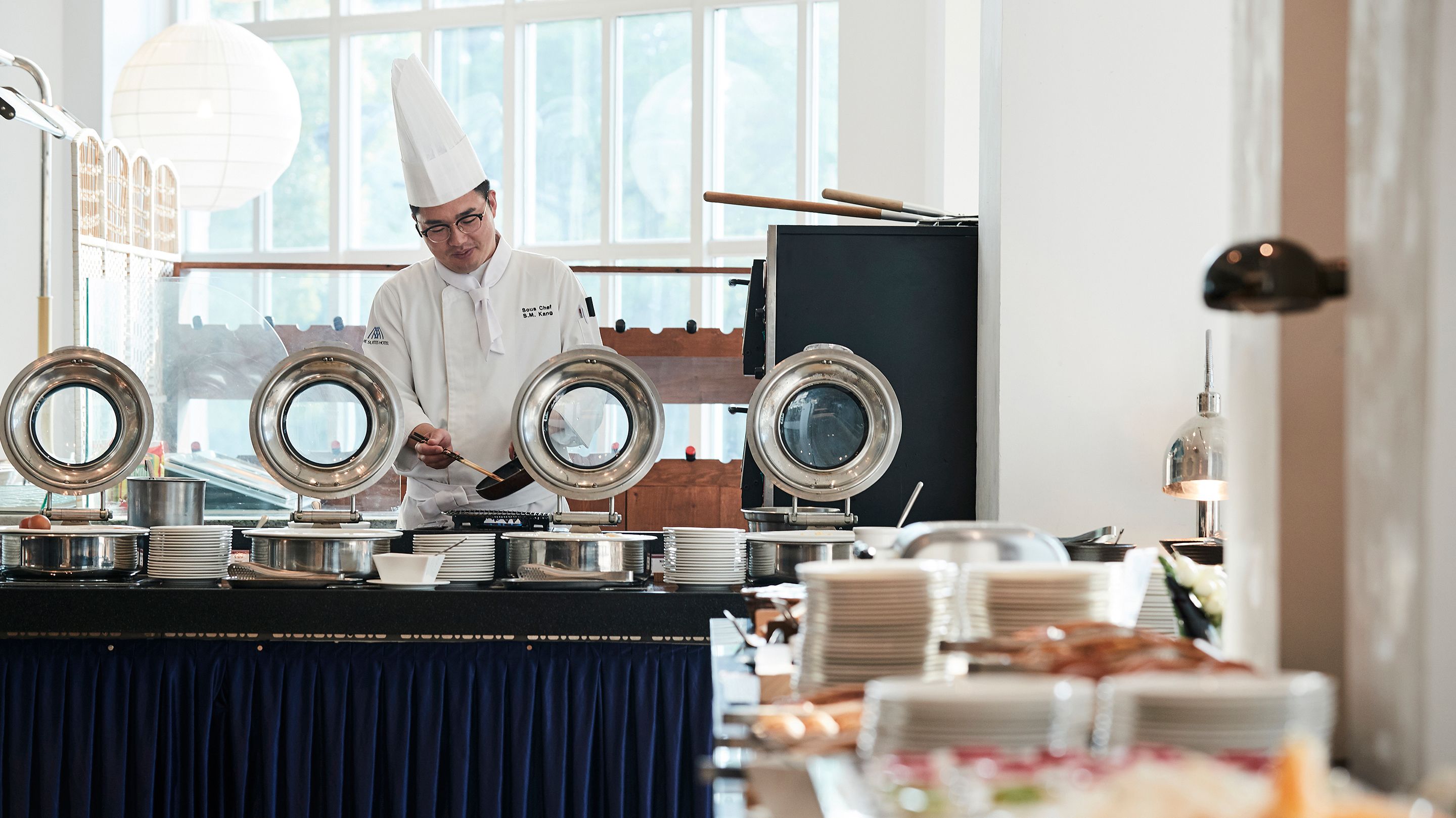 A chef in a white uniform preparing food at a buffet with multiple serving stations.