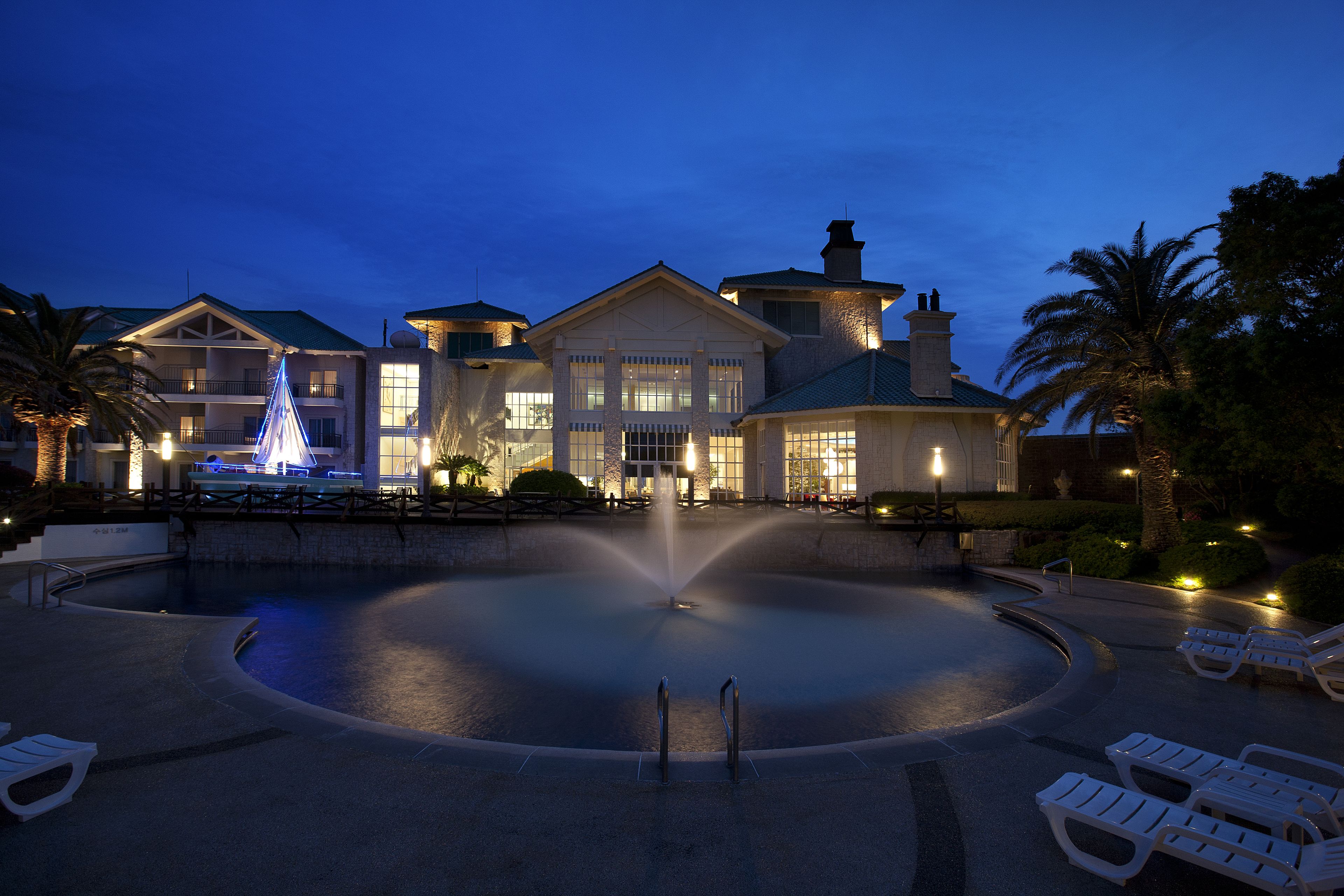 A hotel with a large pool, lounge chairs, and a fountain.