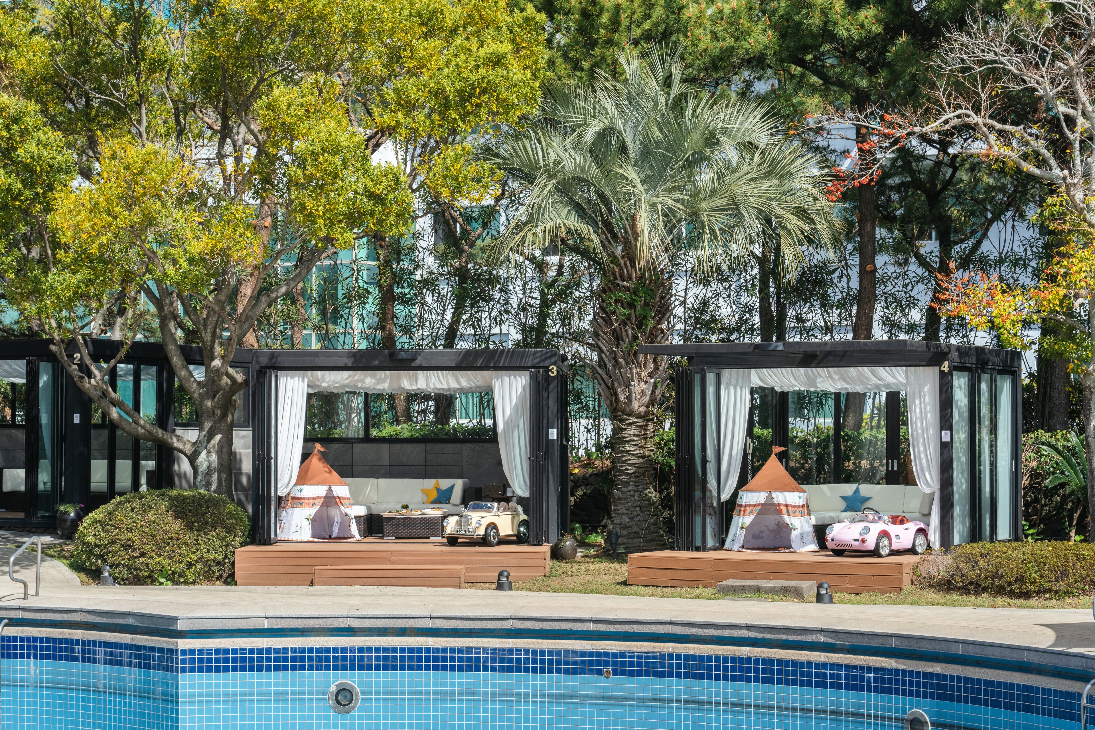 Zona de piscina con dos áreas de descanso cubiertas, cada una decorada con un coche y una estrella.