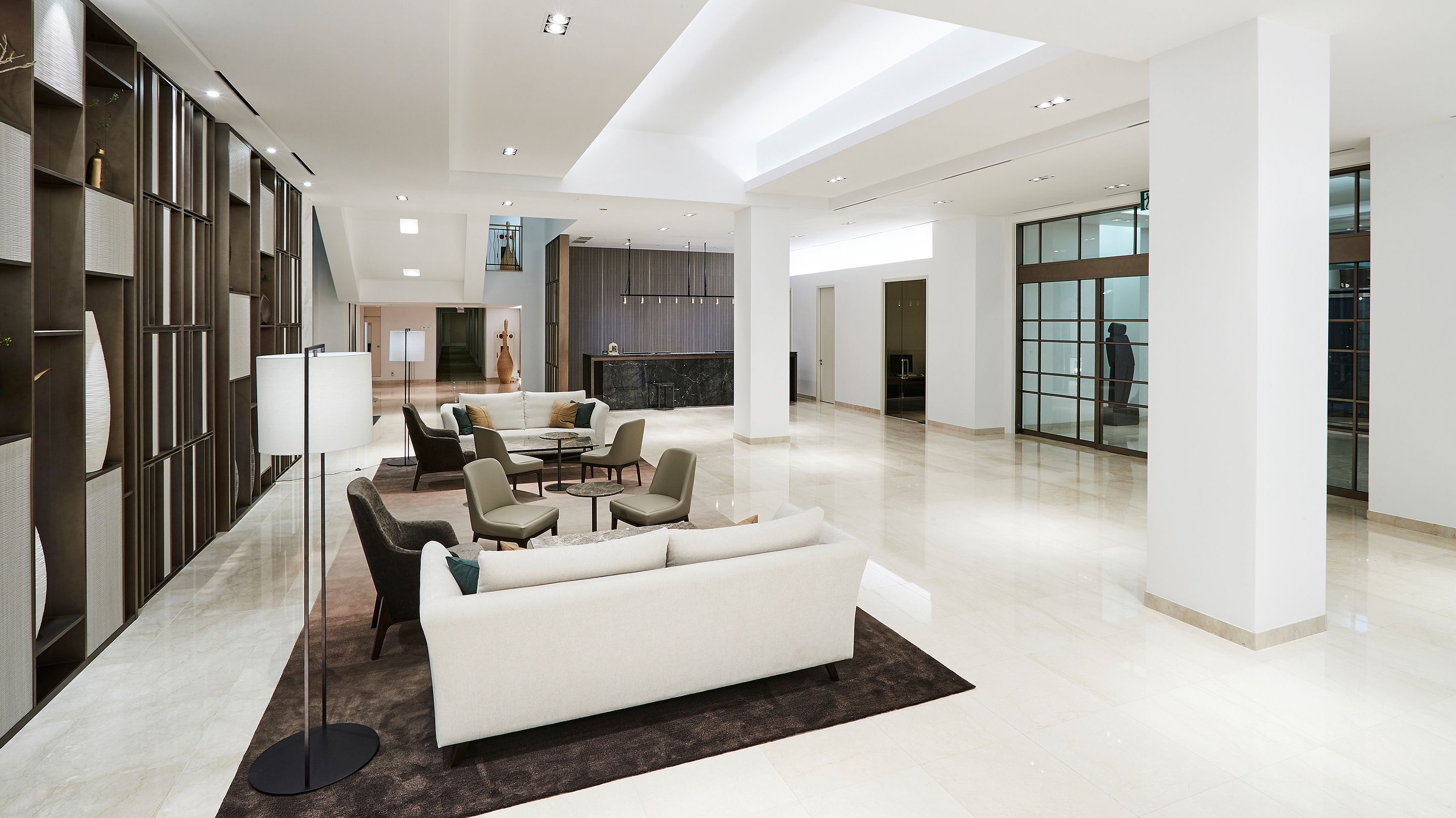 A spacious, modern interior with a central seating area, a kitchen, and a large glass wall providing a view.