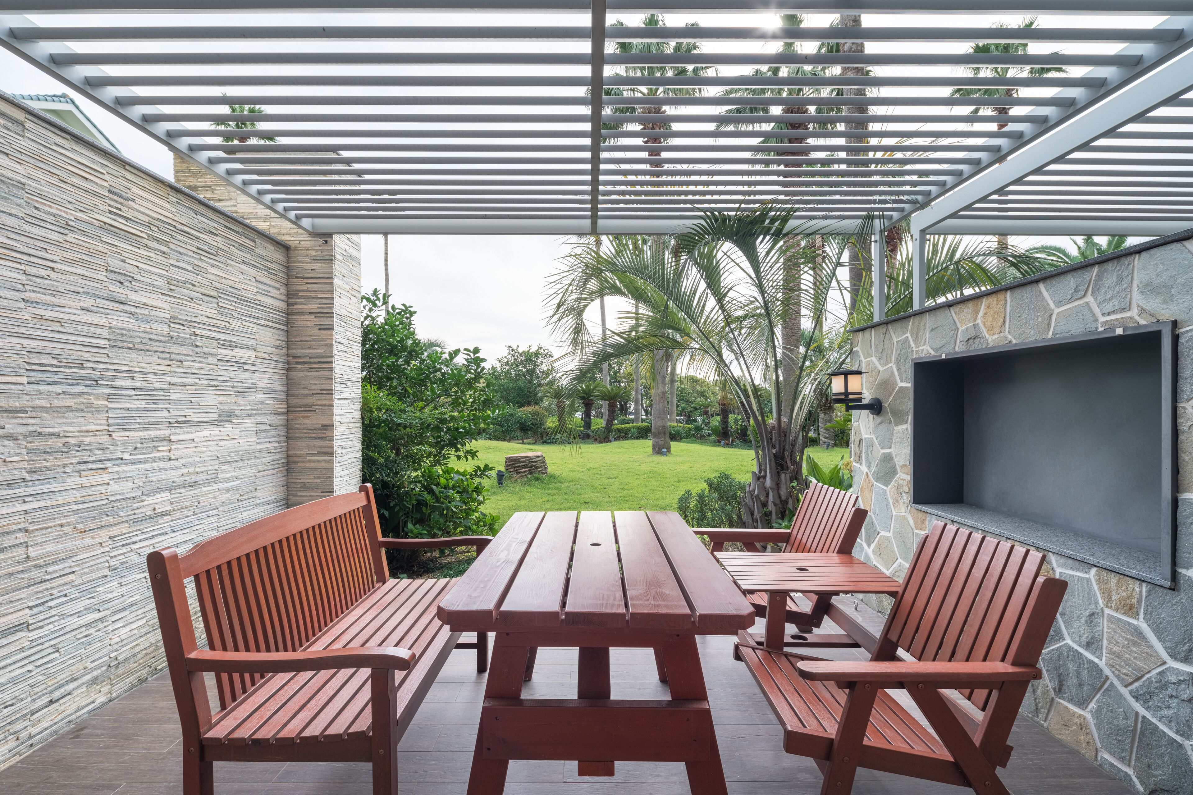 Een terras met een houten tafel en stoelen, een stenen muur en een aan de muur bevestigde televisie.