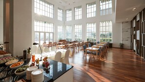 Een ruime eetruimte met hoge plafonds en grote ramen, met meerdere tafels en stoelen voor een diner.