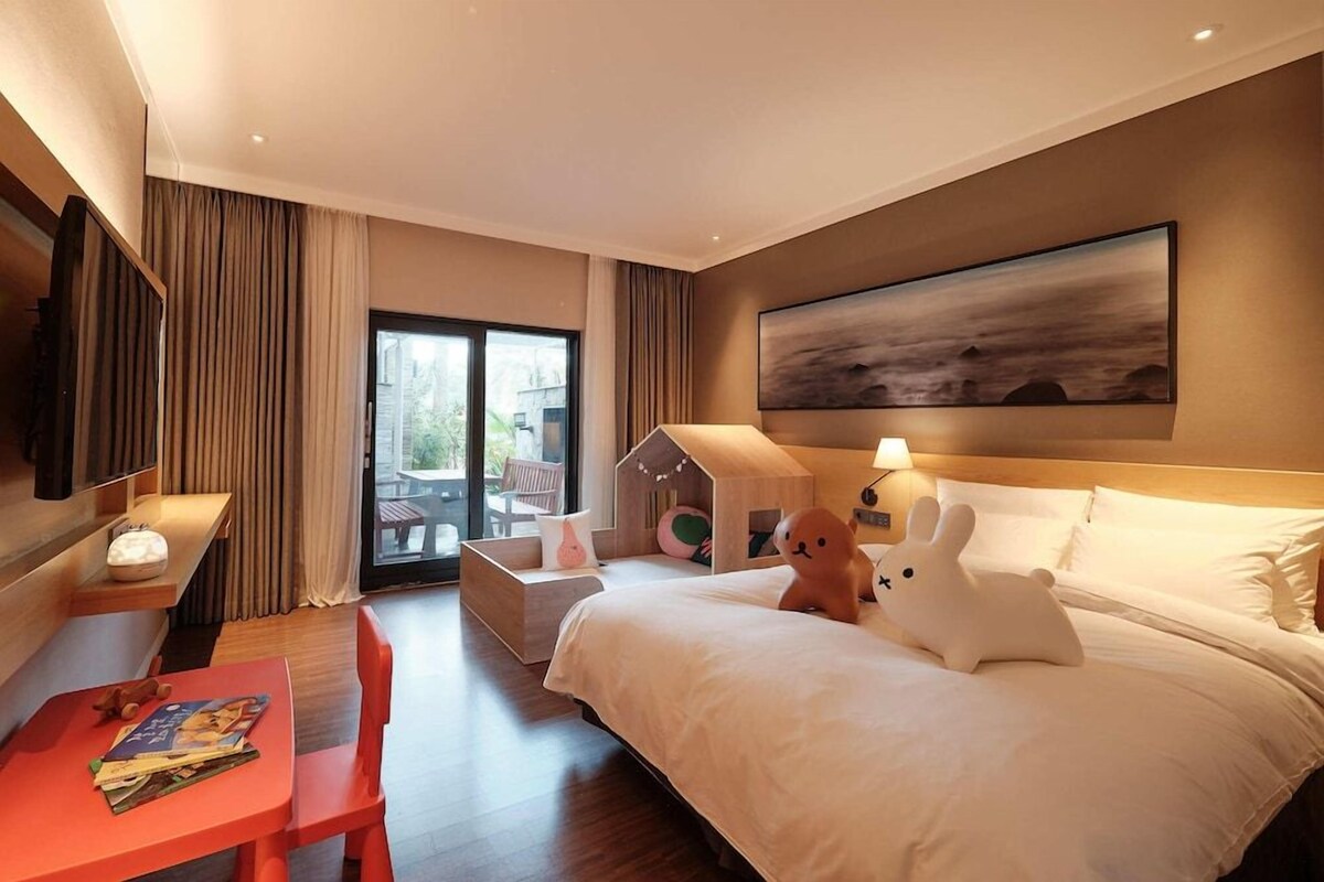 Une chambre d’hôtel avec un lit, une télévision, une table avec une chaise et une fenêtre avec des rideaux.