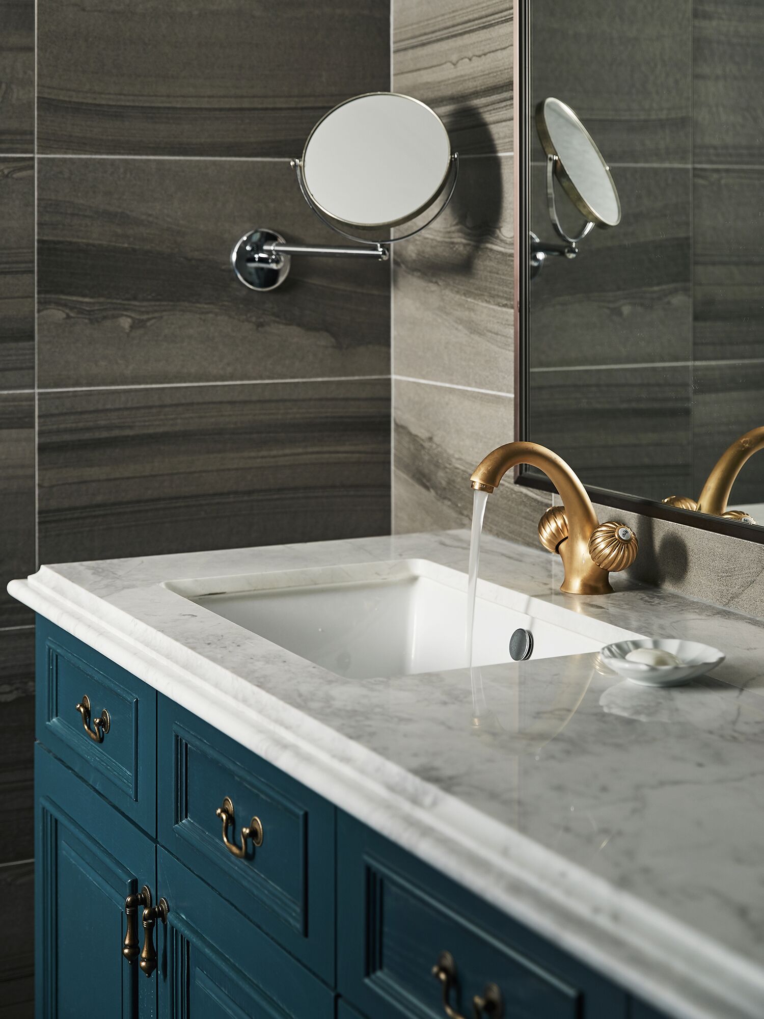 A bathroom with a marble sink, gold faucet, and teal cabinetry.