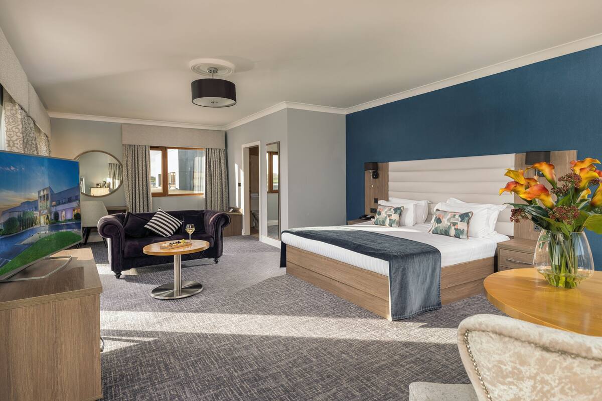 A hotel room with a bed, a sofa, a small table, a TV, and a vase with flowers.