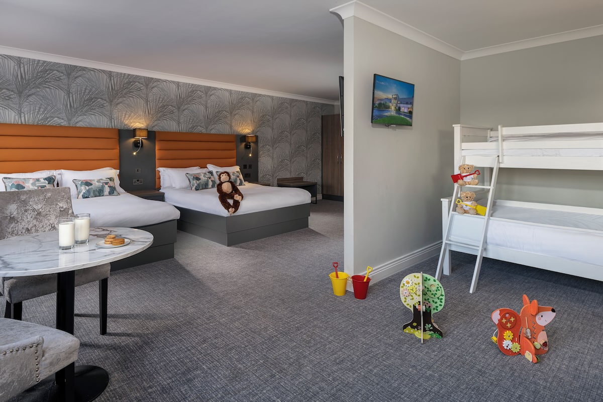 A hotel room with a bed, bedside tables, a small table with drinks, a bunk bed, and children's toys.