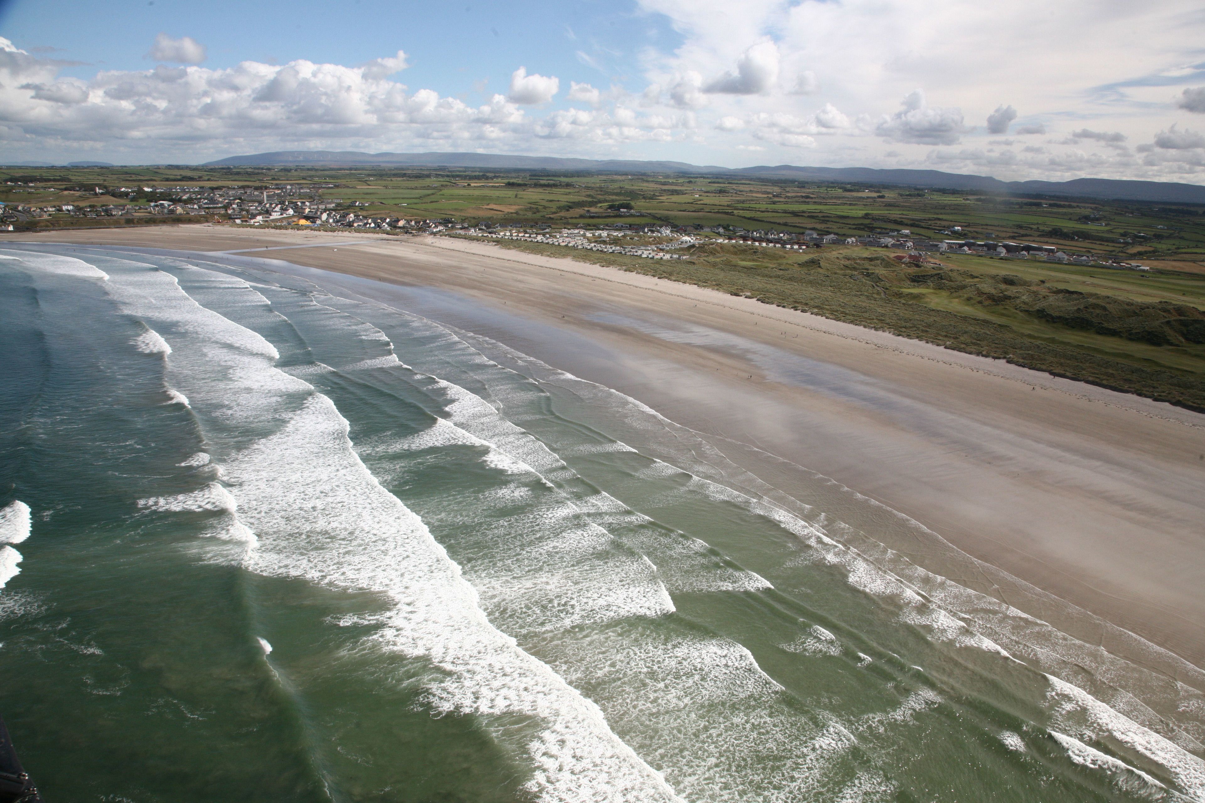 A coastal beach with waves, a sandy shore, and a distant village.