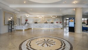 Un vestíbulo de hotel con un mostrador de recepción de mármol, una gran lámpara de araña y un diseño de piso circular.