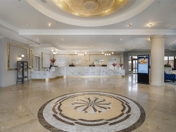 Un vestíbulo de hotel con un mostrador de recepción de mármol, una gran lámpara de araña y un diseño de piso circular.