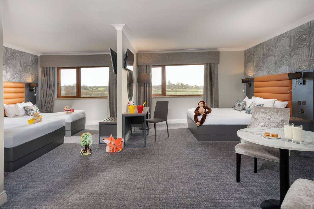 A hotel room with two beds, a desk, a chair, a small table, and a TV.