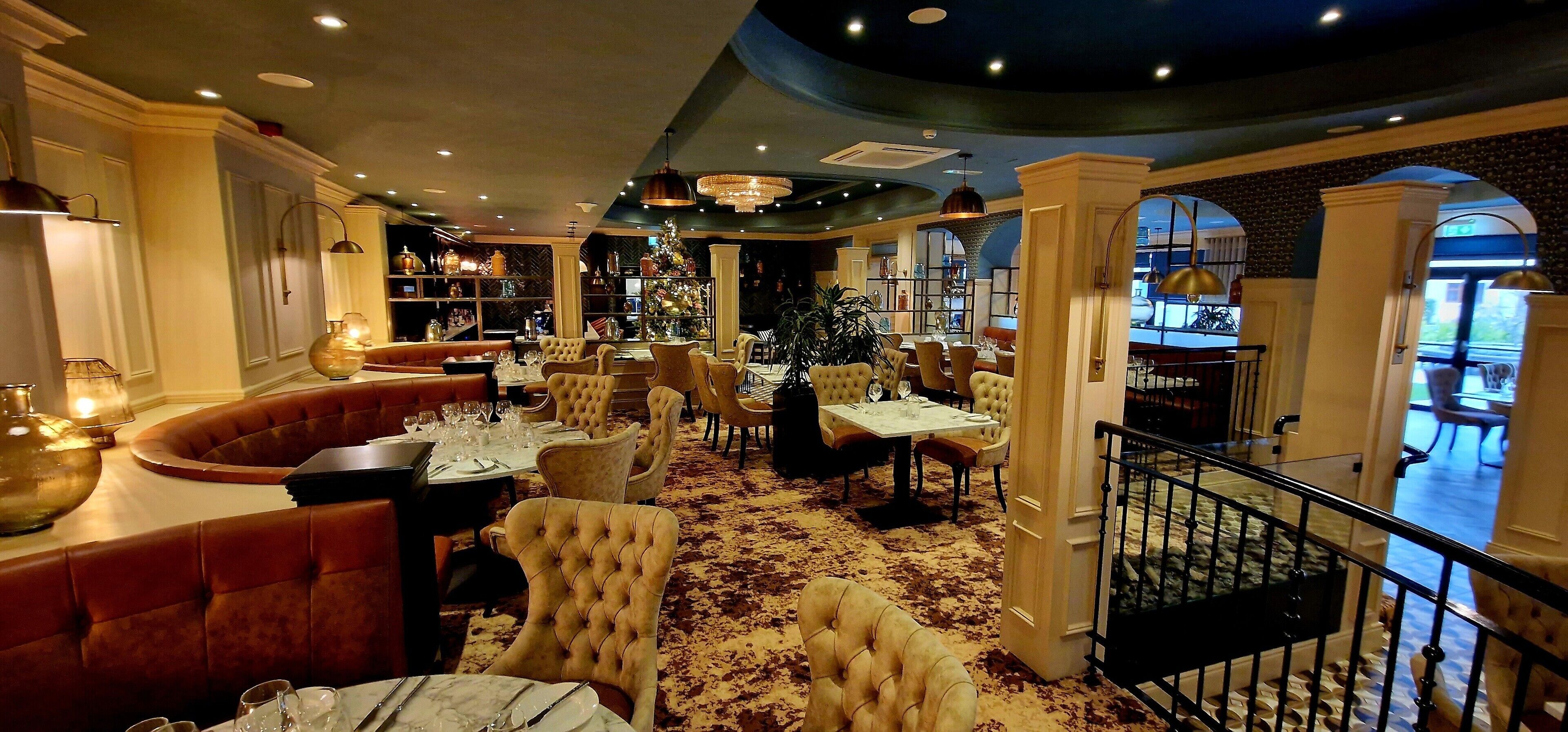 Un restaurant avec des chaises à haut dossier, une table surmontée d’un plateau de marbre et un lustre.