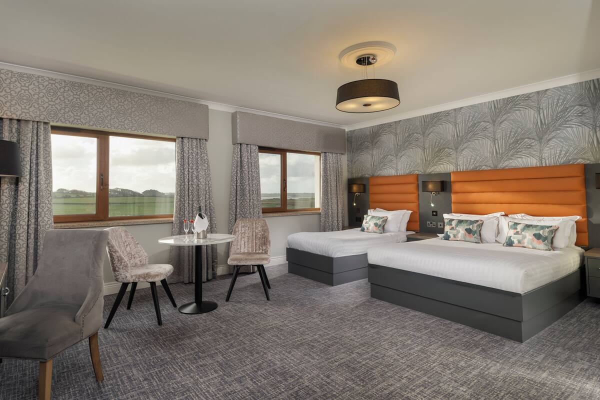 A hotel room with two beds, a small table, a chair, and a view of the outdoors.