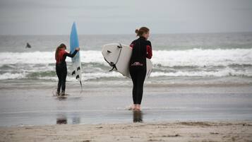 Dos personas cargando tablas de surf en una playa.