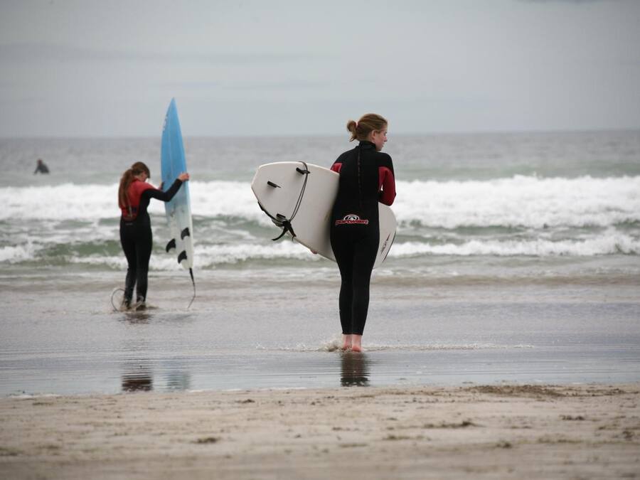 Dos personas cargando tablas de surf en una playa.
