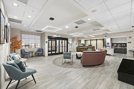 A modern lobby with seating areas, a reception desk, and a kitchen in the background.. Homewood Suites by Hilton Lancaster