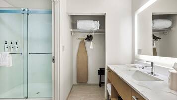 Une salle de bain moderne avec une douche à l’italienne en verre, un lavabo blanc avec un grand miroir et un placard de rangement avec des étagères.
