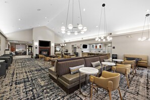 A hotel lobby with a large seating area, a fireplace, and a kitchen visible in the background. - Homewood Suites by Hilton Lancaster (Lancaster)