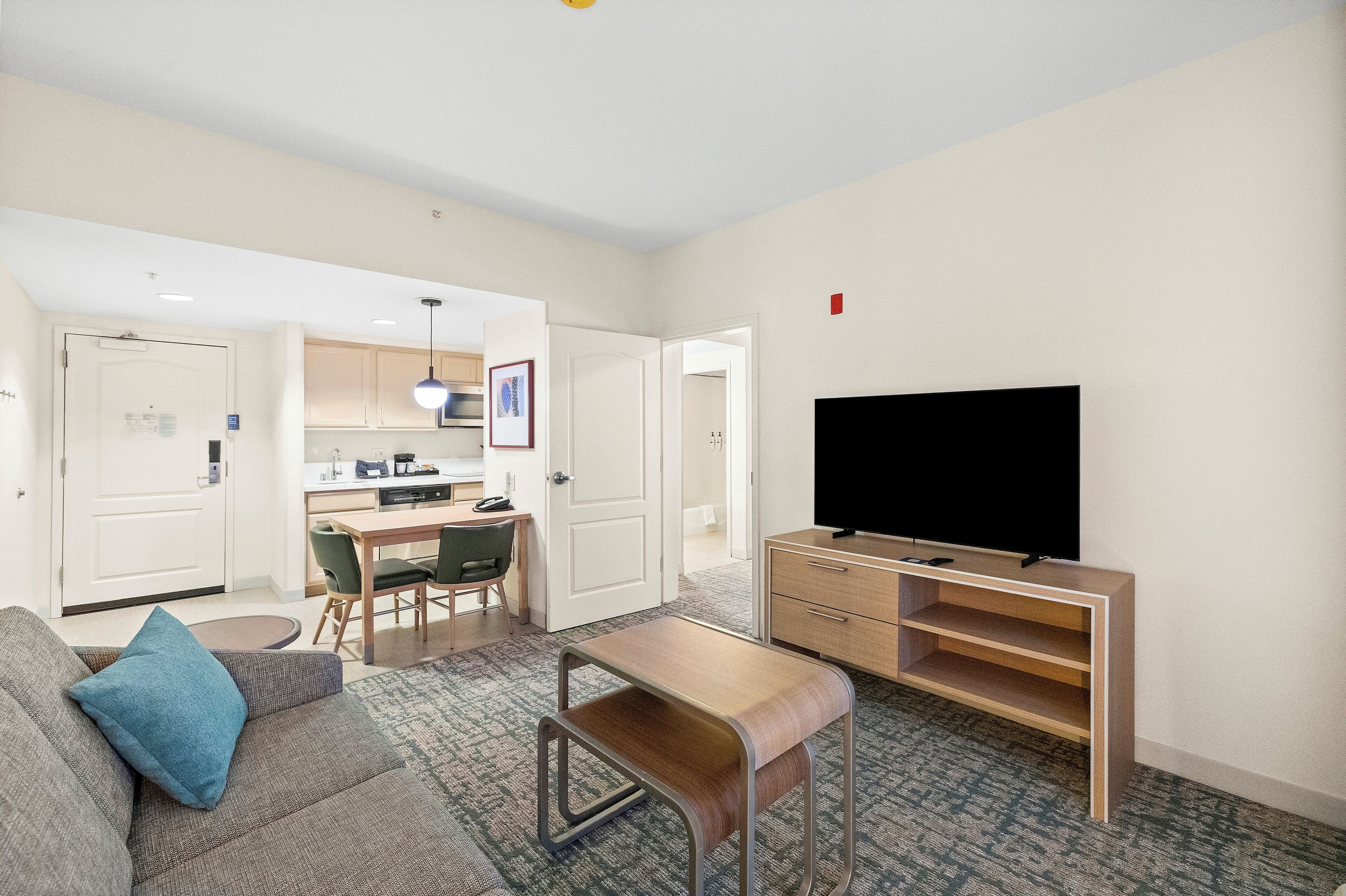 A modern living room with a sofa, a coffee table, a TV, and a dining area with chairs and a table.