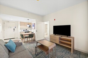 A modern living room with a sofa, a coffee table, a TV, and a dining area with chairs and a table.