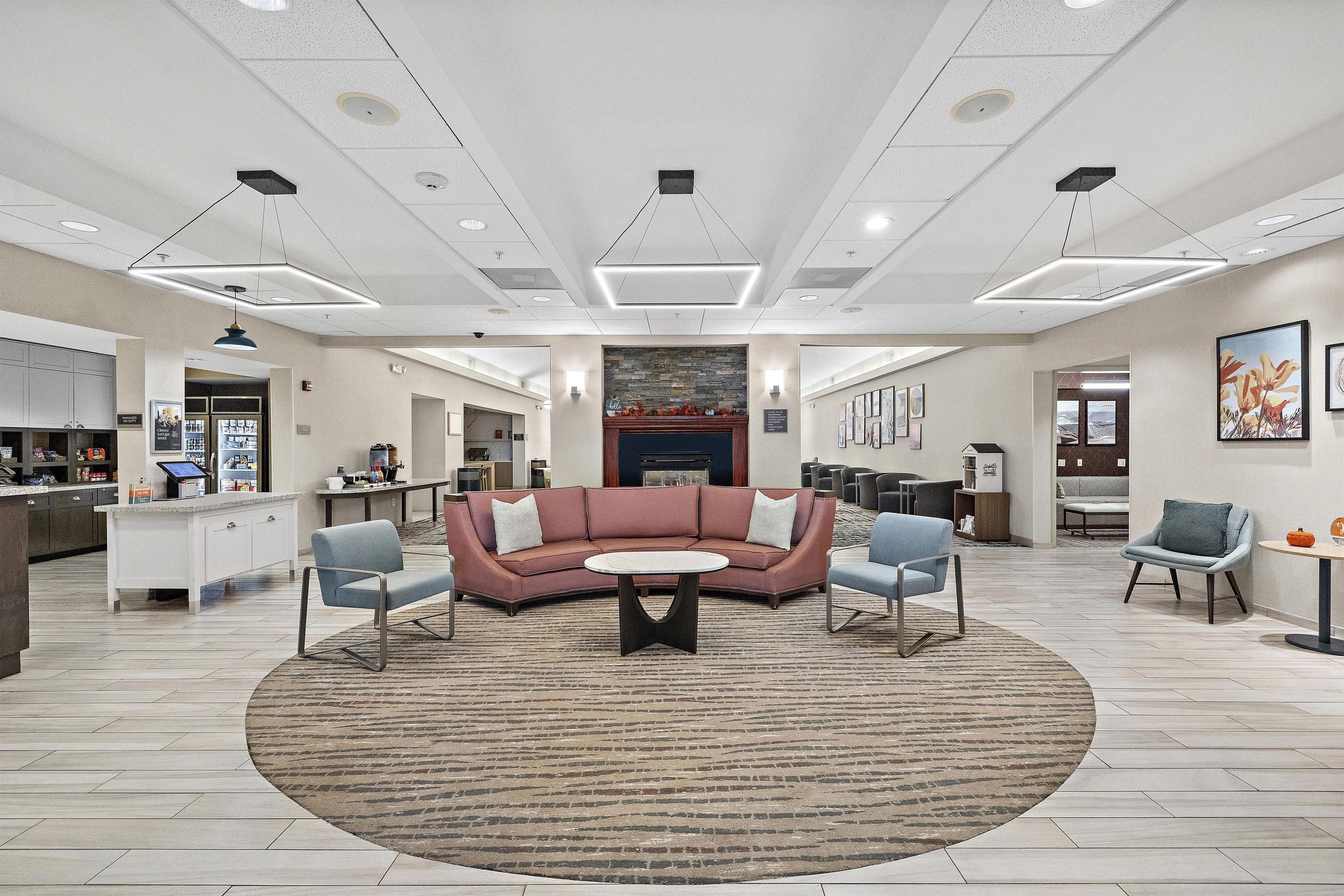 A spacious lobby with a central seating area, a kitchen in the background, and a fireplace.
