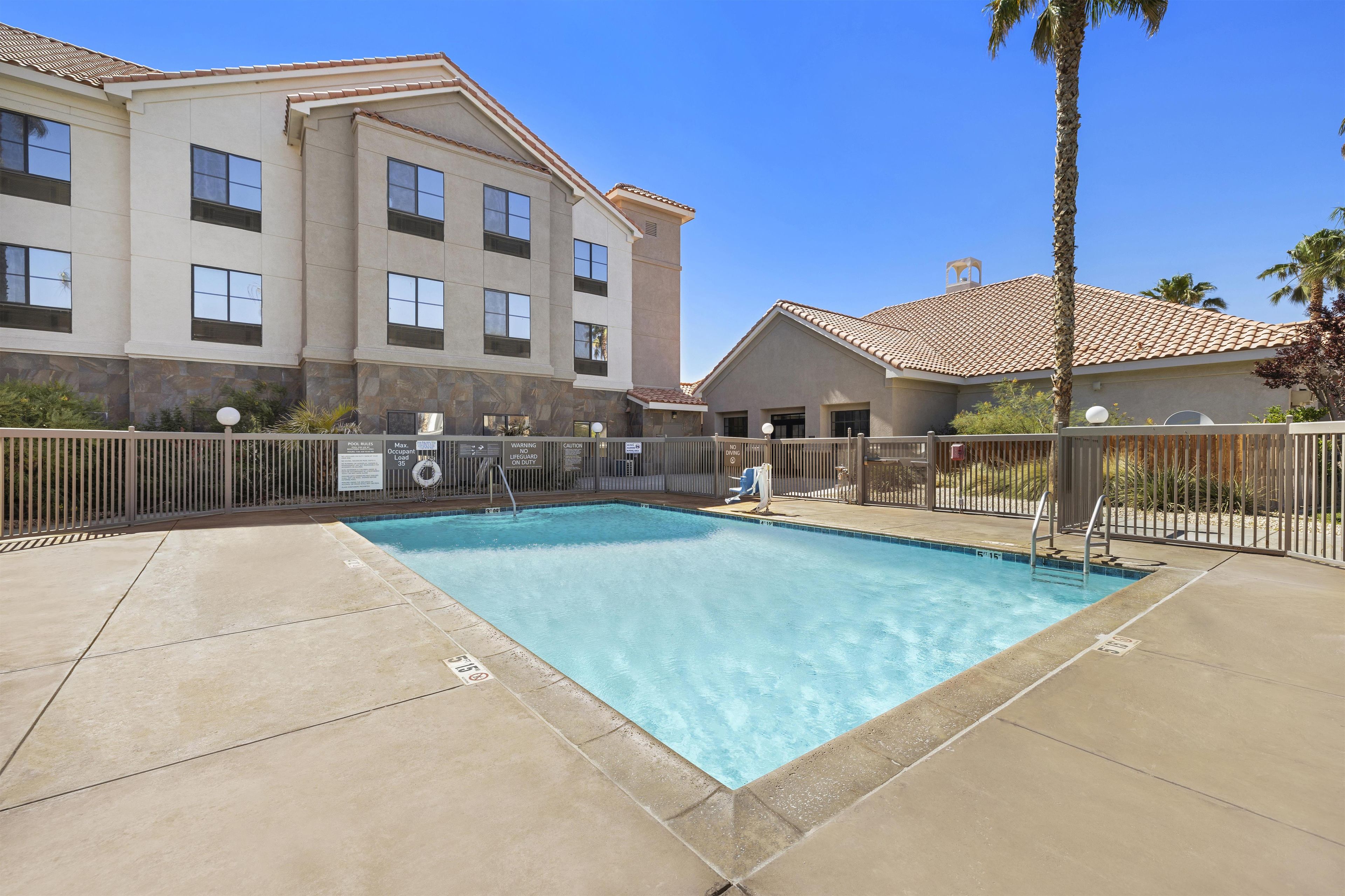 A swimming pool with a tiled deck, a building with multiple windows, and a palm tree.