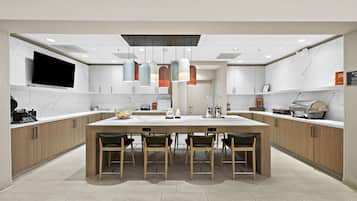 A modern kitchen with a central island, pendant lights, and a flat-screen TV.