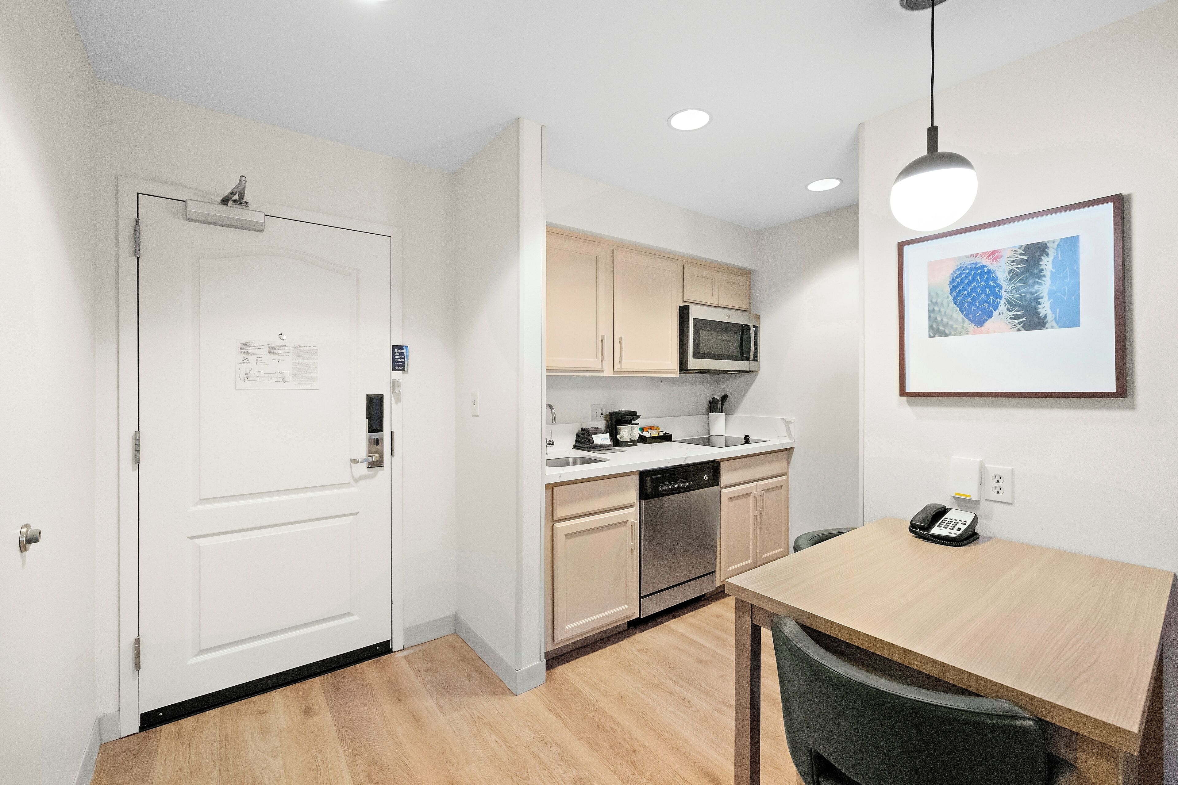 A compact kitchen with white cabinets, a microwave, a dishwasher, and a wooden dining table.