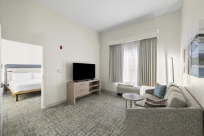 A hotel room with a bed, a TV on a stand, a sofa, a small table, and a window with curtains. - Homewood Suites by Hilton Lancaster (Lancaster)