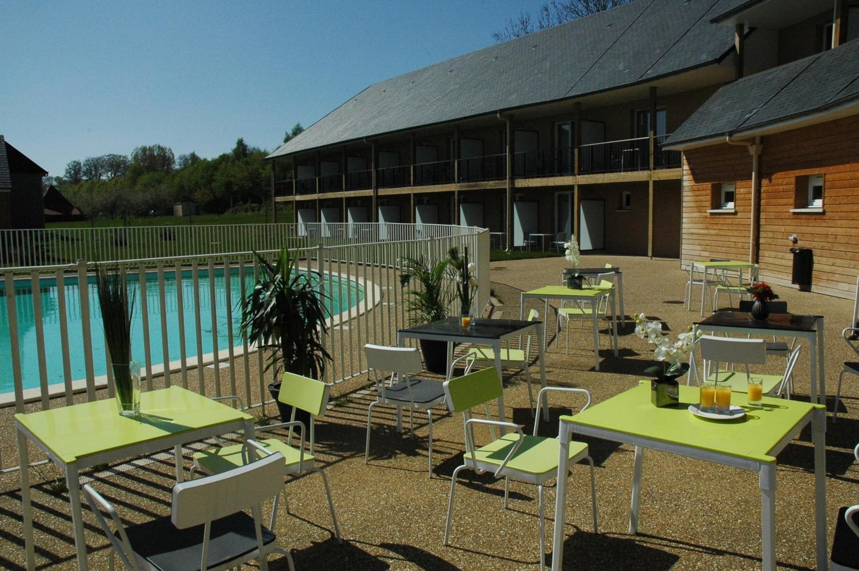 Uma área à beira da piscina com mesas e cadeiras, uma piscina e um edifício com várias varandas.