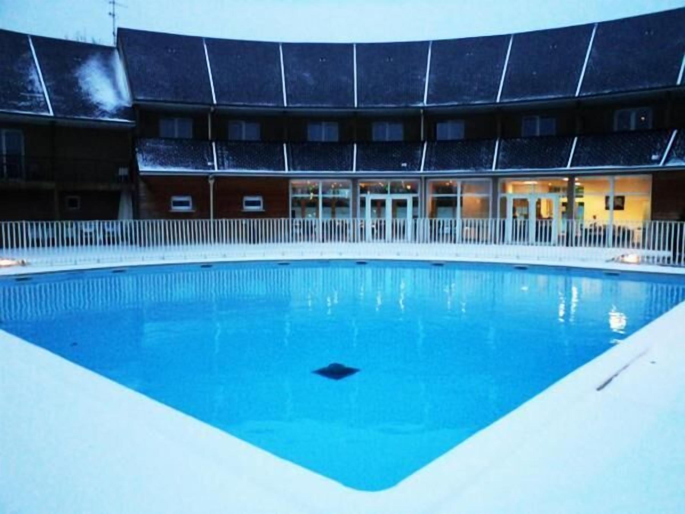 A swimming pool with a white deck and a building with multiple windows in the background.