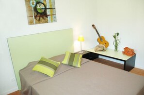 Una habitación con una cama, una guitarra, una lámpara y un florero con flores.