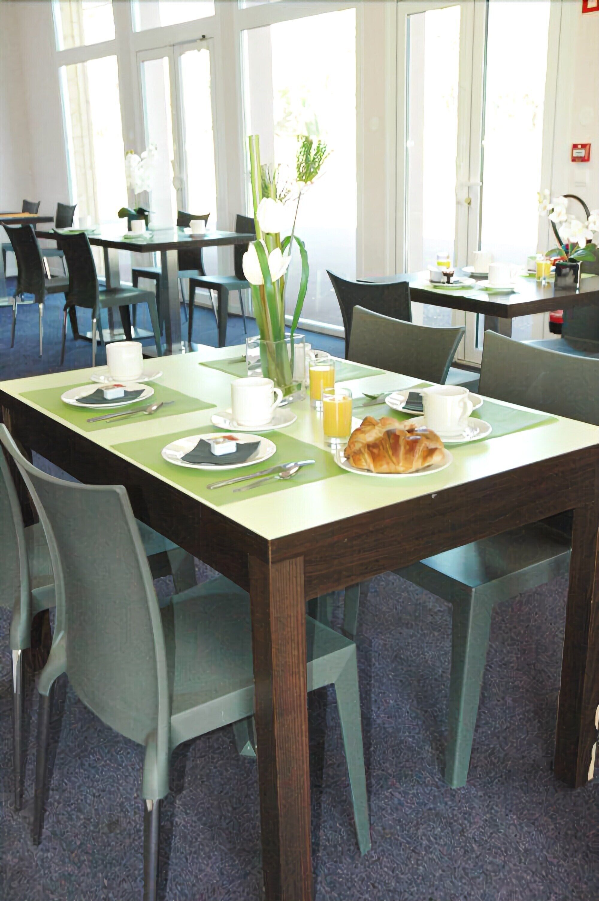 A dining area with tables set for breakfast, including plates, cups, and a croissant.