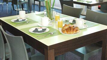 A dining area with tables set for breakfast, including plates, cups, and a croissant.