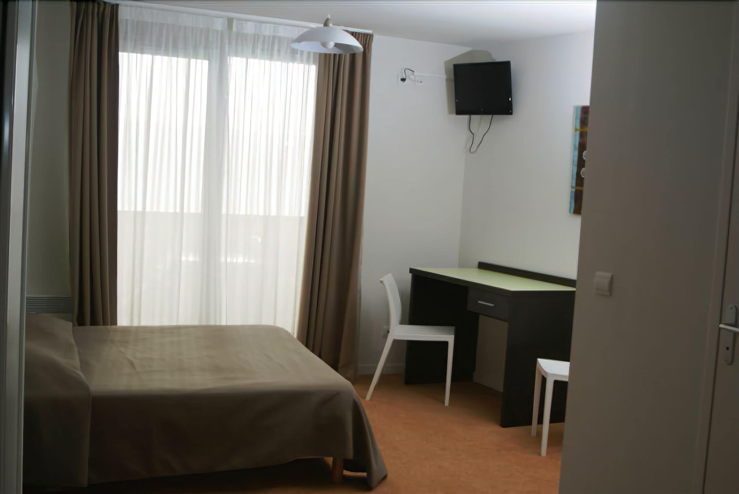 Una habitación de hotel con una cama, un escritorio, una silla y un televisor en la pared.