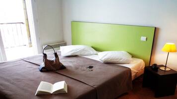 A hotel room with a bed, a bedside table, a lamp, and a handbag on the bed.