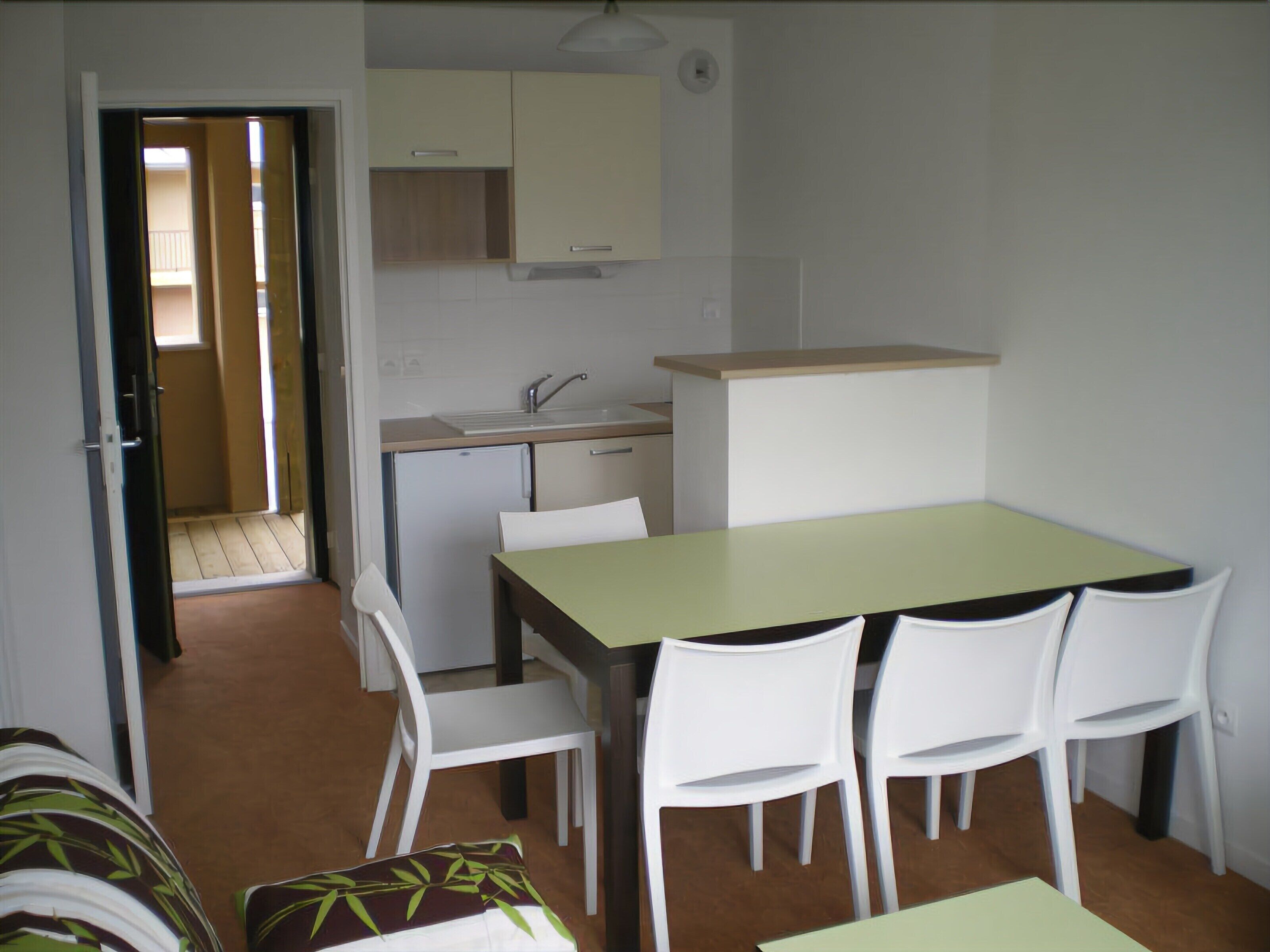 A compact kitchen with a dining area, including a table and chairs, and a small refrigerator.