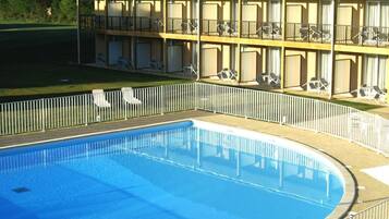 Una piscina con valla blanca, rodeada de sillas de descanso y un edificio con balcones.