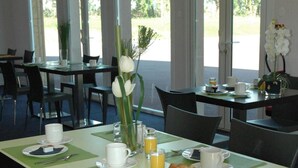 Un área de desayuno con mesas dispuestas para dos personas, equipada con platos, tazas, cubiertos y un croissant.