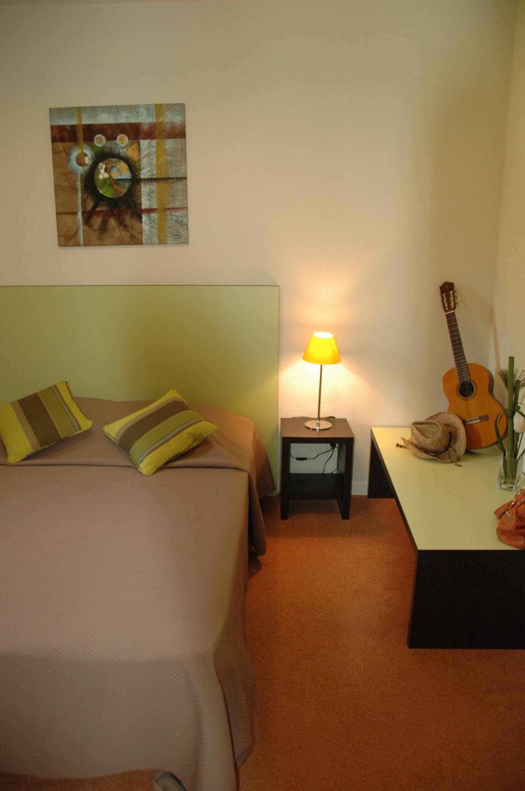 Une chambre à coucher avec un lit, des oreillers, une lampe, une guitare et un tableau accroché au mur.