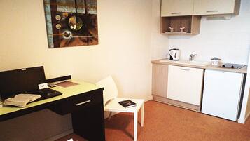 Una habitación de hotel compacta con kitchenette, escritorio, silla y cama.
