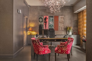 Un comedor moderno con una mesa larga, dos sillas tapizadas rojas, una silla de oficina negra y decoración en la pared.