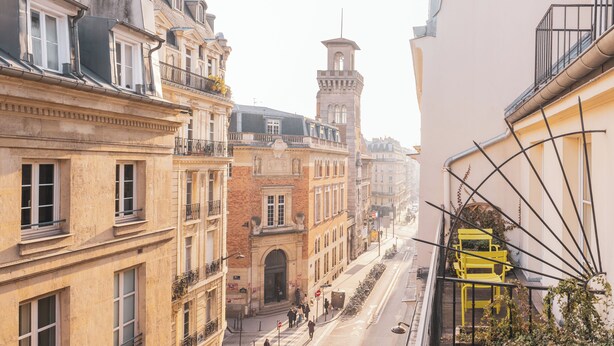 A street view with buildings, a tower, and a yellow chair on a balcony. - Hotel Le Petit Paris (Paris)