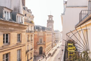 Vista de la calle con edificios, una torre y una silla amarilla en un balcón.