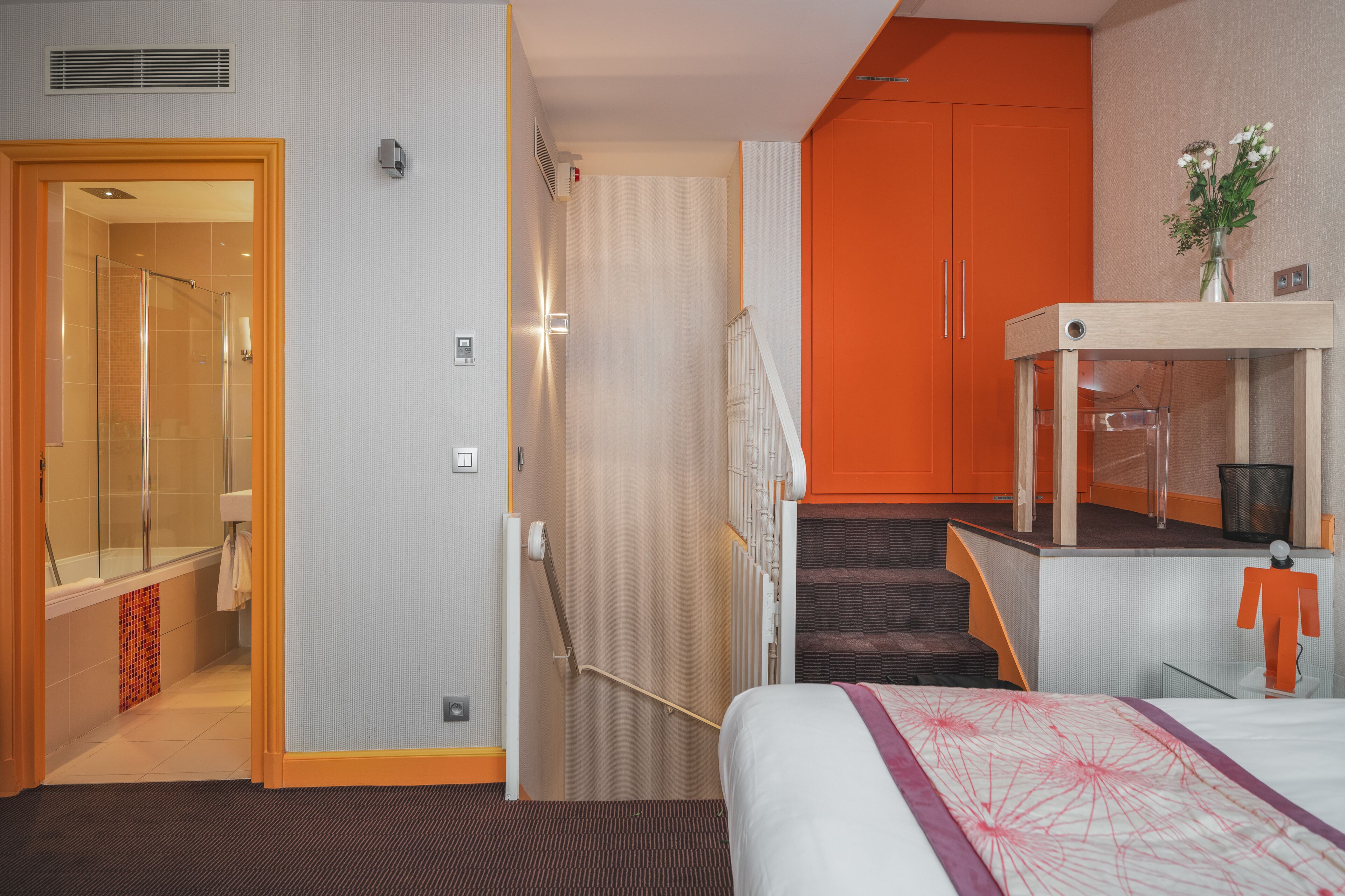 A hotel room with a bed, a shower, a staircase, and a small table with a vase.