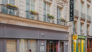 A hotel facade with ornate architectural details, a signboard, and storefronts with visible signage. - Hotel Le Petit Paris (Paris)